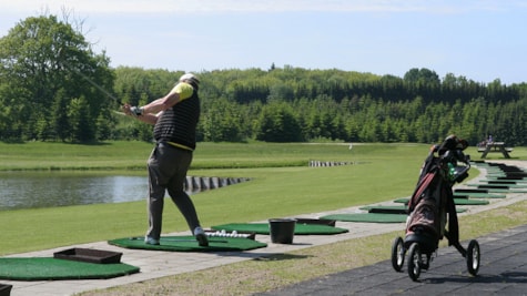 En golfspiller øver sit slag på Langesø golfbane med Langesøskoven i baggrunden