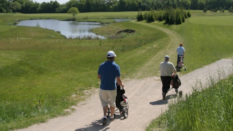 Tre golfspillere går på stien på golfbanen med en lille sø i baggrunden