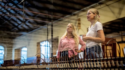 To voksne kvinder står og kigger på en gammel industriel væv på museumshallen Tekstilfabrikken ved Industrimuseet i Horsens Jylland